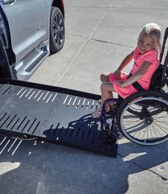 Smiling girl in wheelchair on vehicle side ramp
