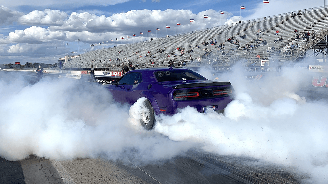 Purple Dodge Challenger smoking its tires on a drag strip