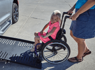 Smiling girl in wheelchair on vehicle side ramp
